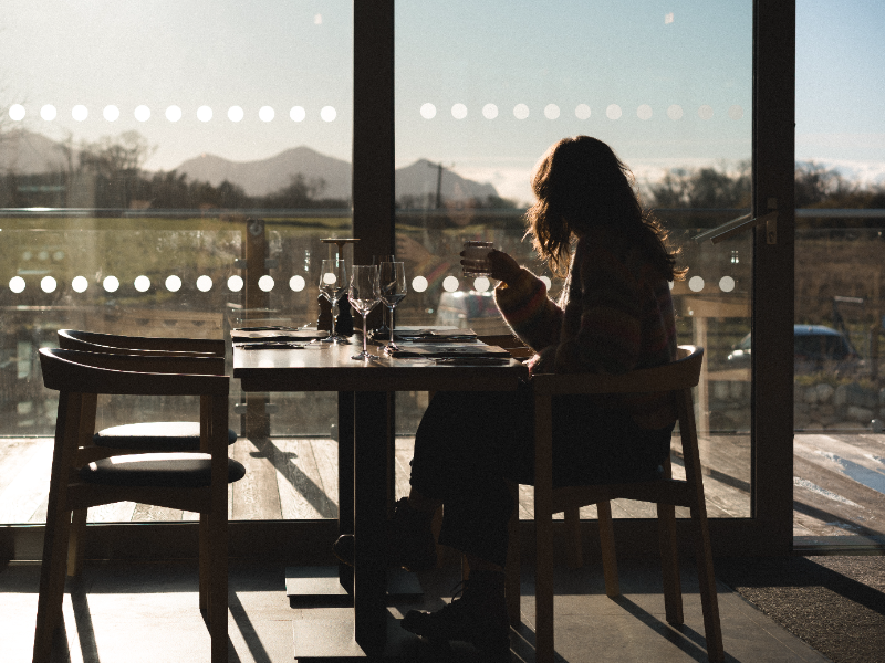 A woman chat drinking a coffee looking out of a window to a view of mountains